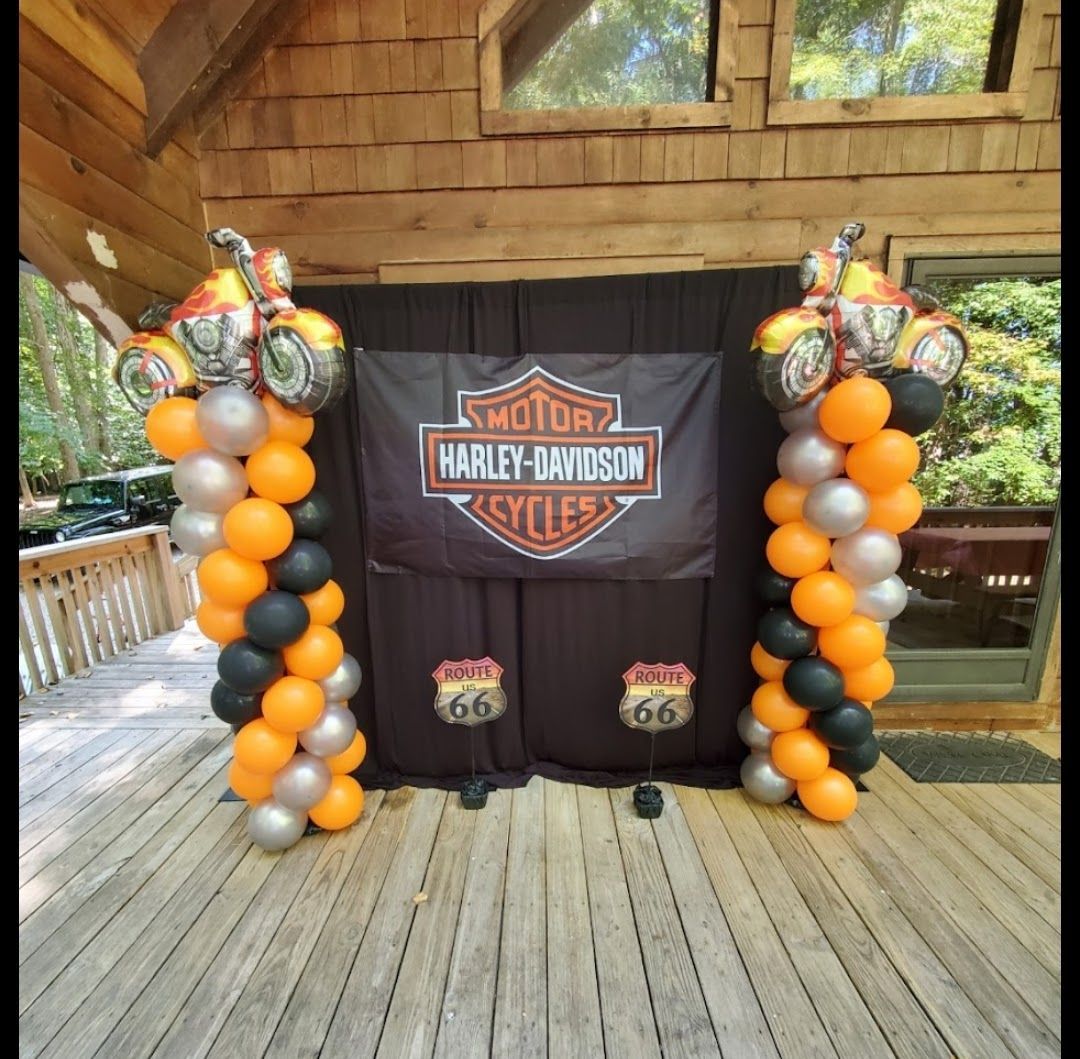 Harley-Davidson themed backdrop on a wooden deck featuring balloon columns in orange, black, and silver with motorcycle balloons.