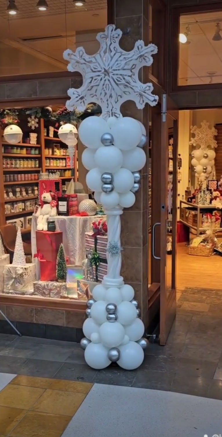 A holiday balloon column made of white balloons and silver accents, topped with a large, glittery snowflake decoration.