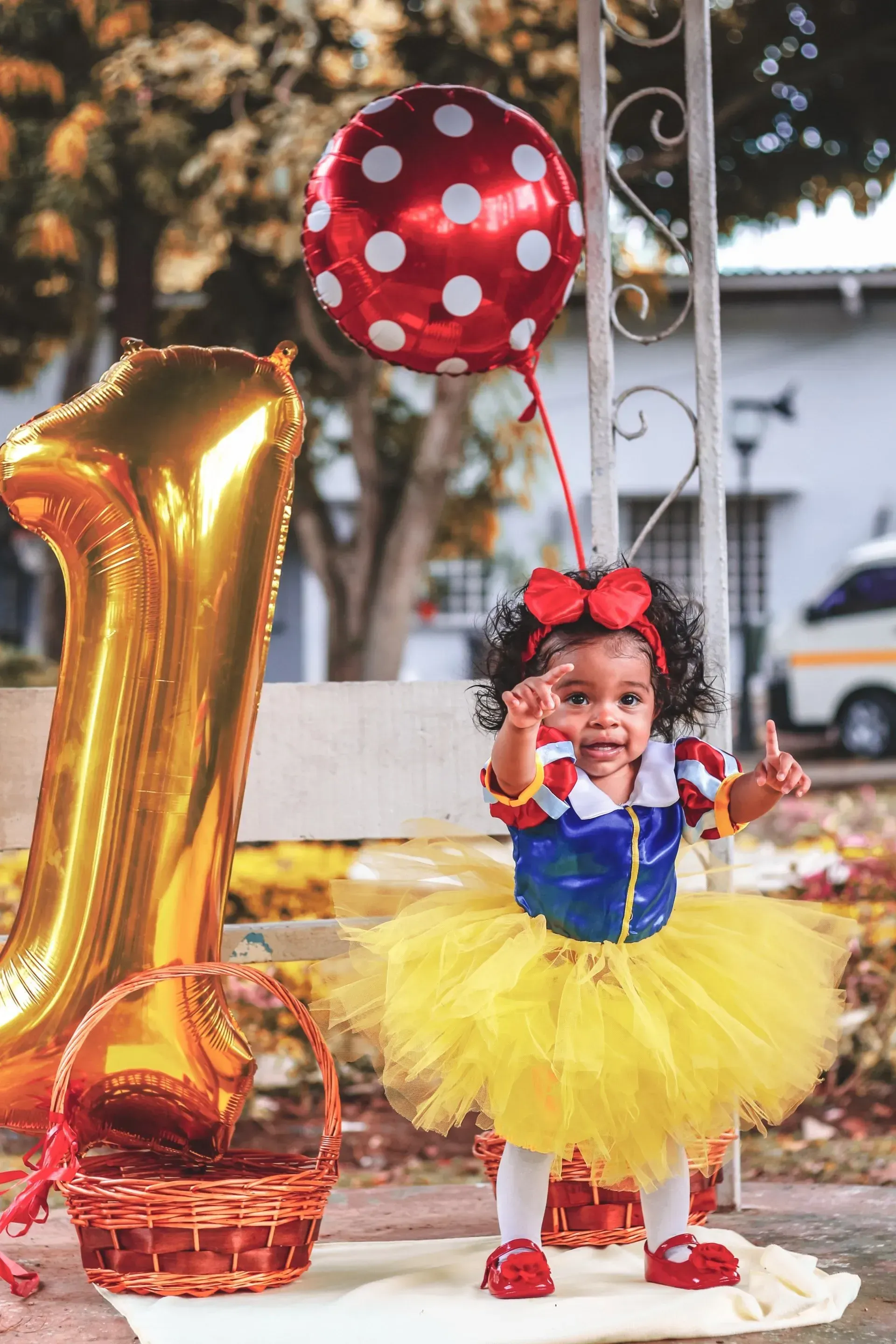 A toddler dressed as Snow White celebrates her first birthday. She is in a yellow tutu with a gold
