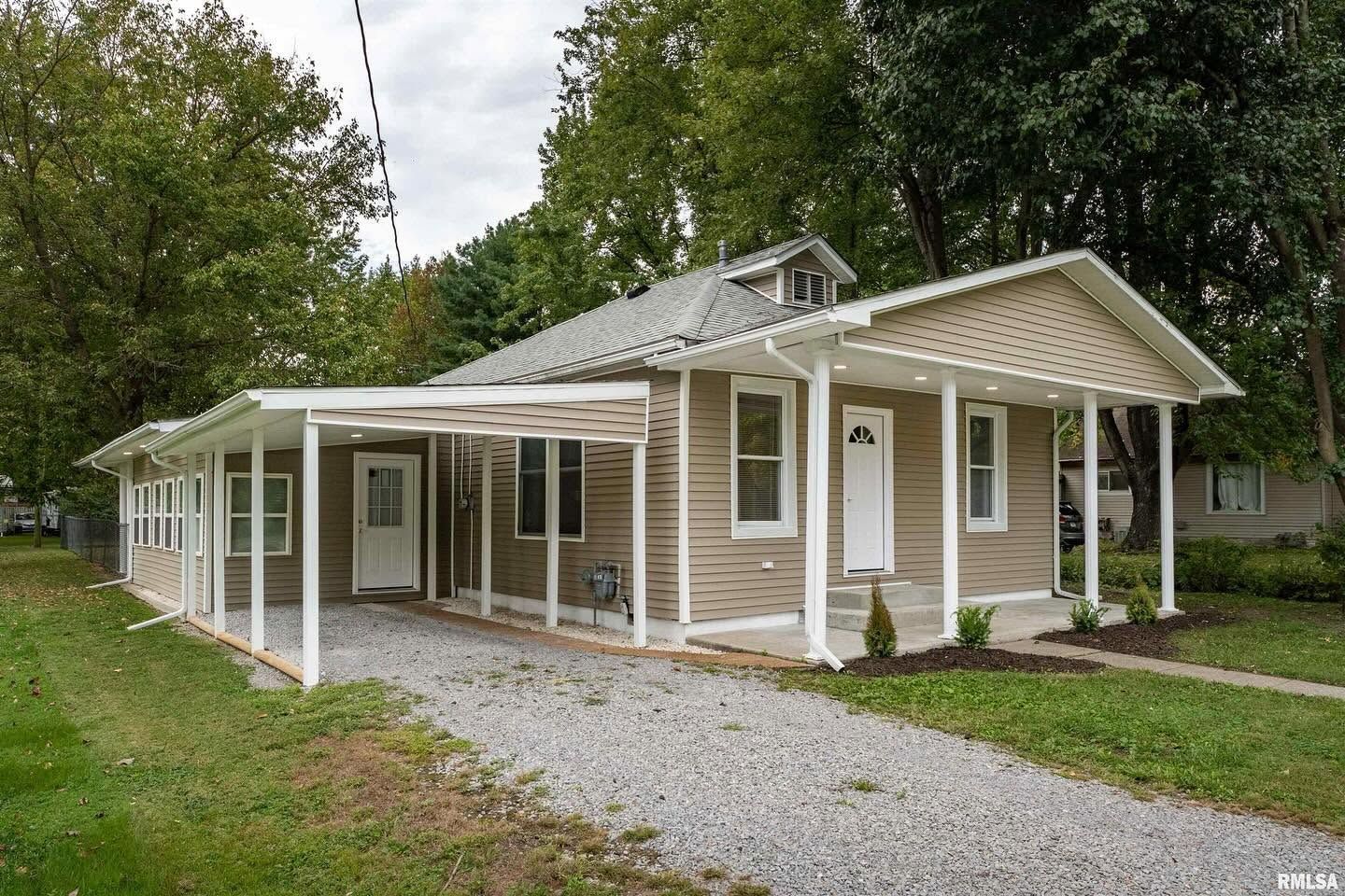 White house with a covered porch, gravel driveway, and trees surrounding the yard