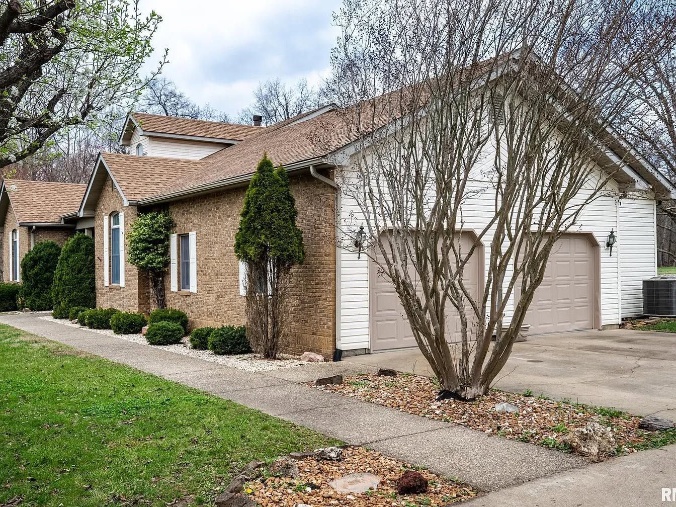 Suburban brick house with white garage, leafless trees, and a driveway in front yard