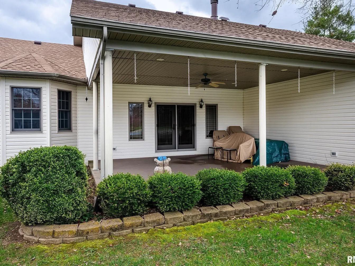 Covered front porch with white siding, double doors, wicker chairs, and trimmed bushes in front of a house.