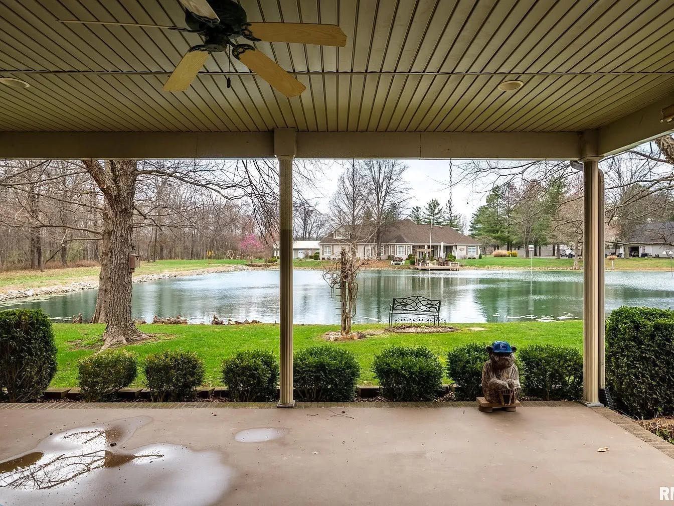 Covered patio overlooking a pond and fountain, with trimmed bushes and wet concrete in the foreground