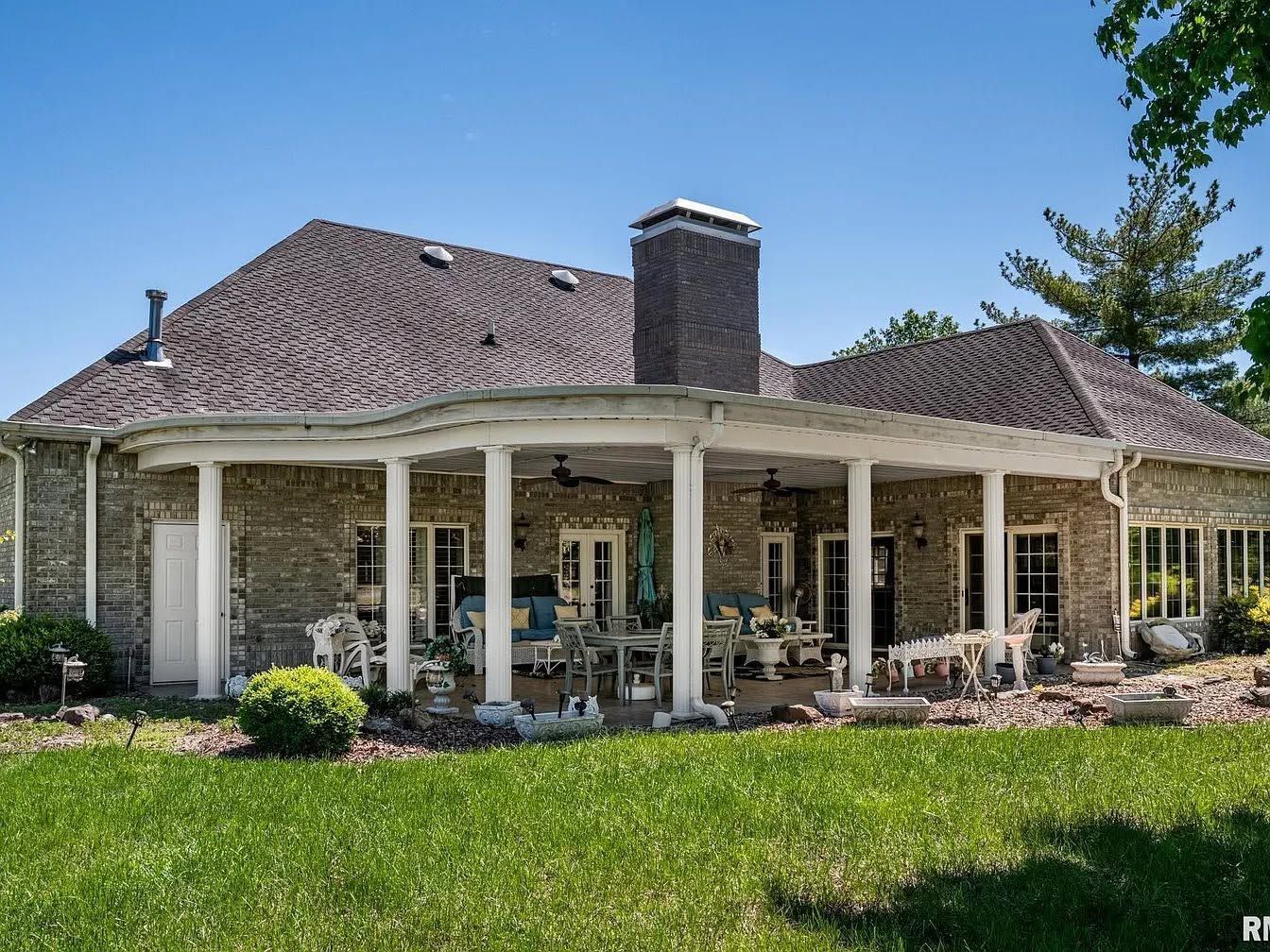 Brick house with a covered patio, white columns, and a green lawn under a clear blue sky