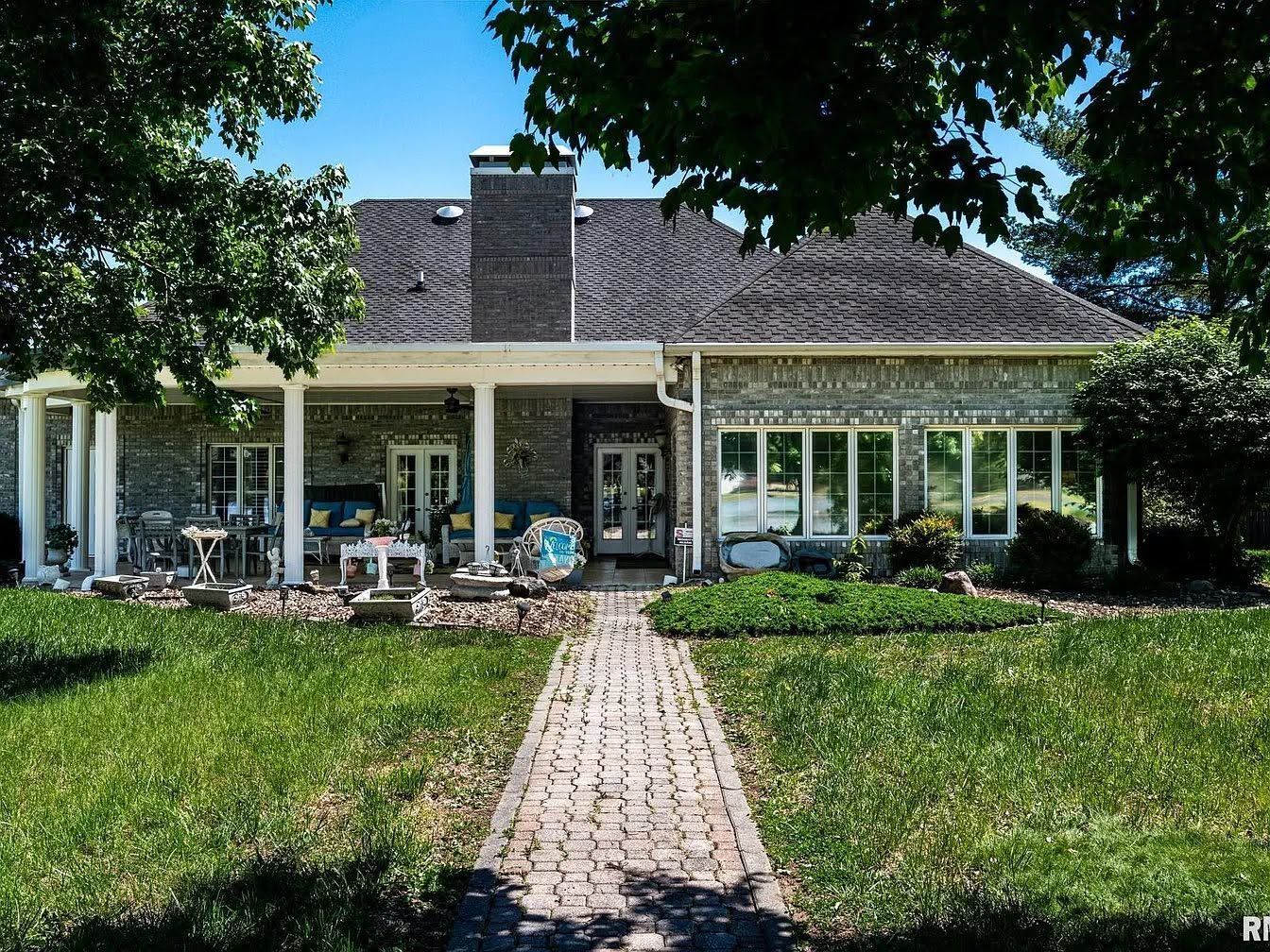 Brick house with a front lawn, patio chairs, and a stone walkway under trees