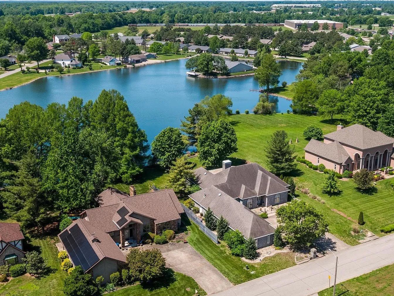 Aerial view of lakeside homes with green trees, a blue lake, and a residential neighborhood.