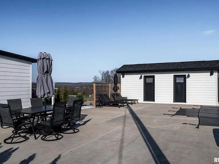 Patio with black metal table and chairs, closed umbrella, and a small white building under a clear blue sky