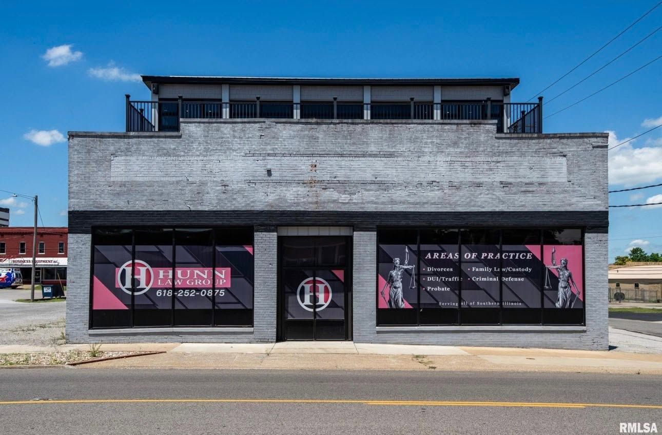 Gray two-story storefront with large pink-and-black window graphics under a blue sky