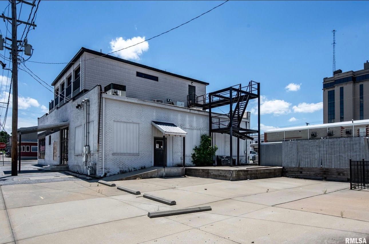 Abandoned industrial building with white walls and metal framework under a blue sky.