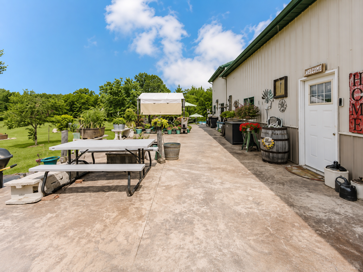 Outdoor patio beside a white building with picnic tables, potted plants, and a sunny blue sky.