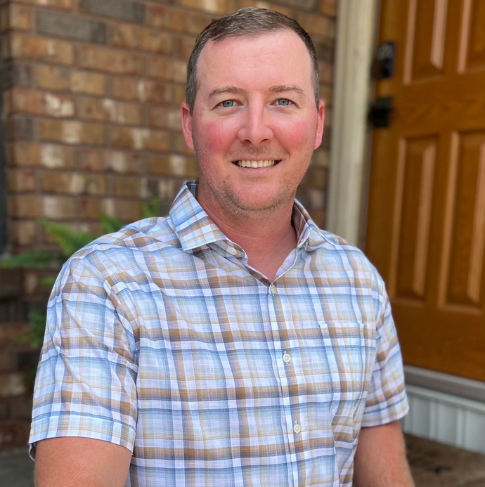 Smiling man in a plaid shirt standing in a doorway outside a house