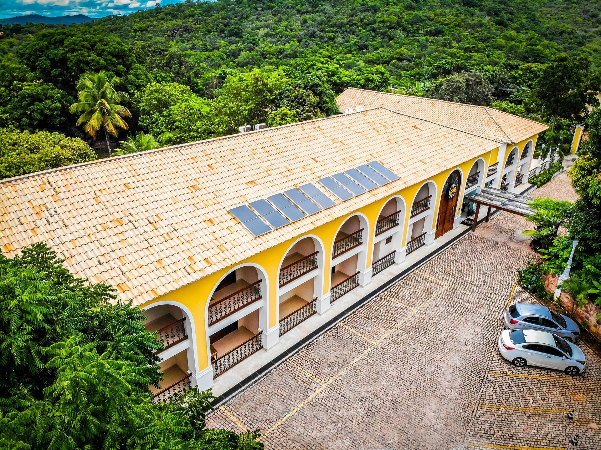 Uma vista aérea de um grande edifício com painéis solares no telhado cercado por árvores.