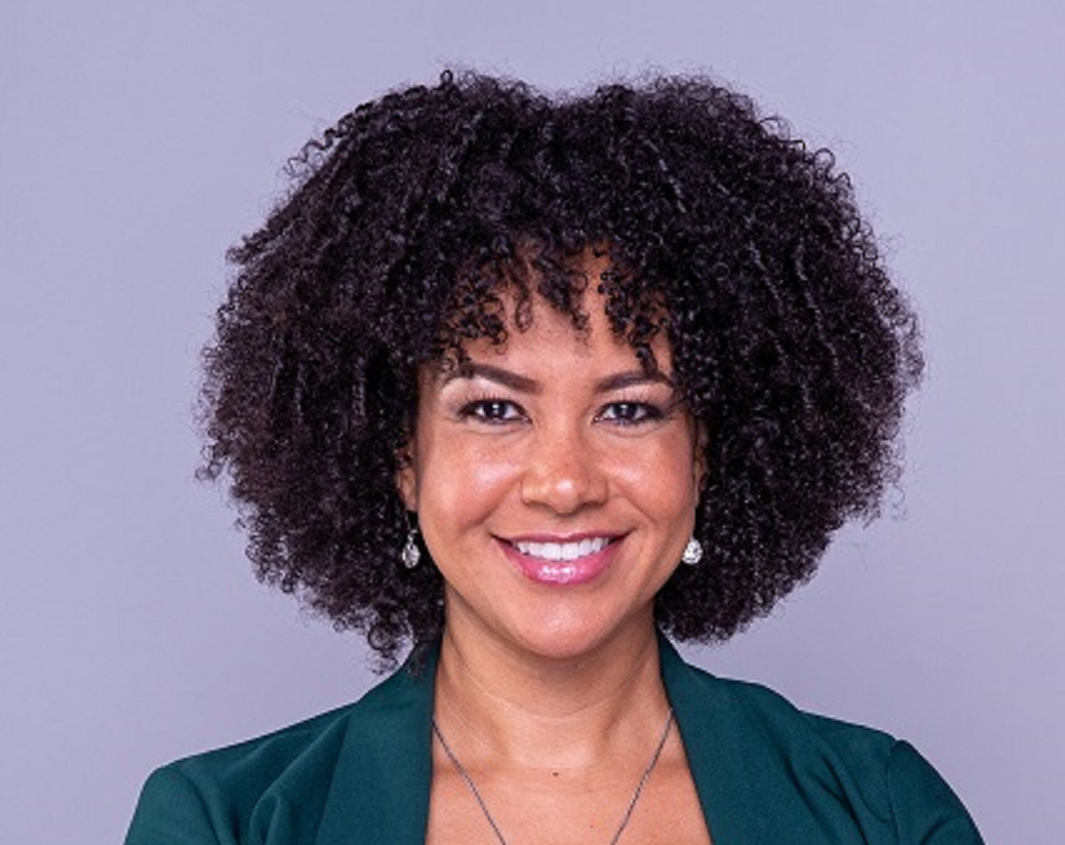 A woman with curly hair is smiling and wearing a green jacket.