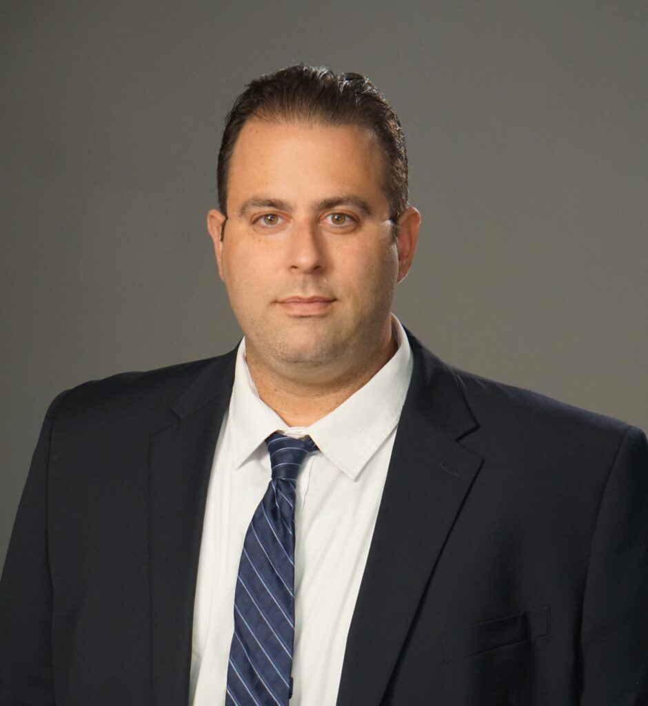 A man in a suit and tie is standing in front of a gray background.