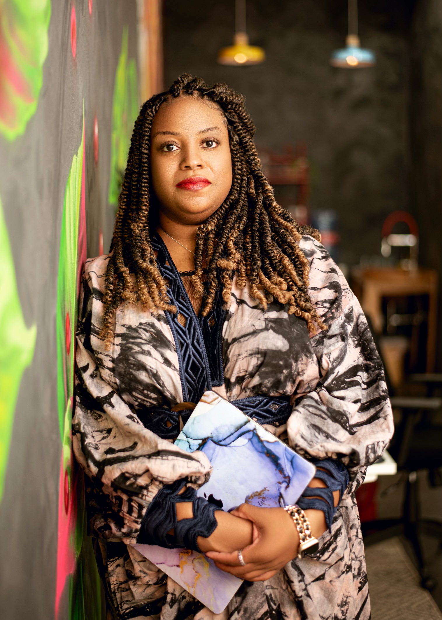A woman is leaning against a wall holding a book.