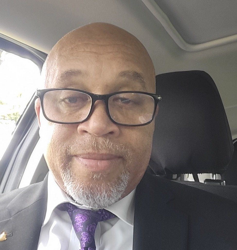 A bald man wearing glasses and a purple tie is sitting in a car