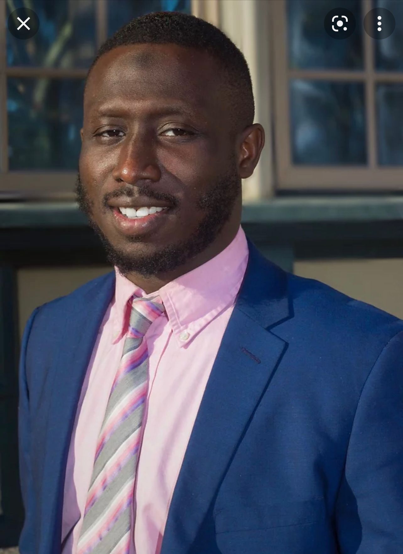 A man in a blue suit and pink shirt is smiling for the camera.