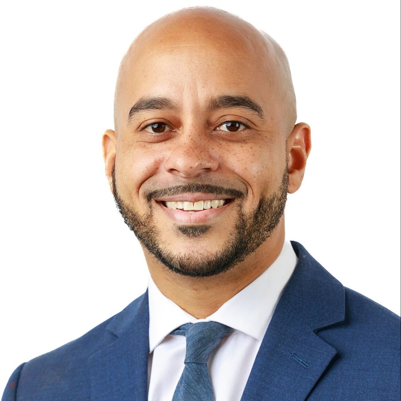 A bald man with a beard wearing a blue suit and tie