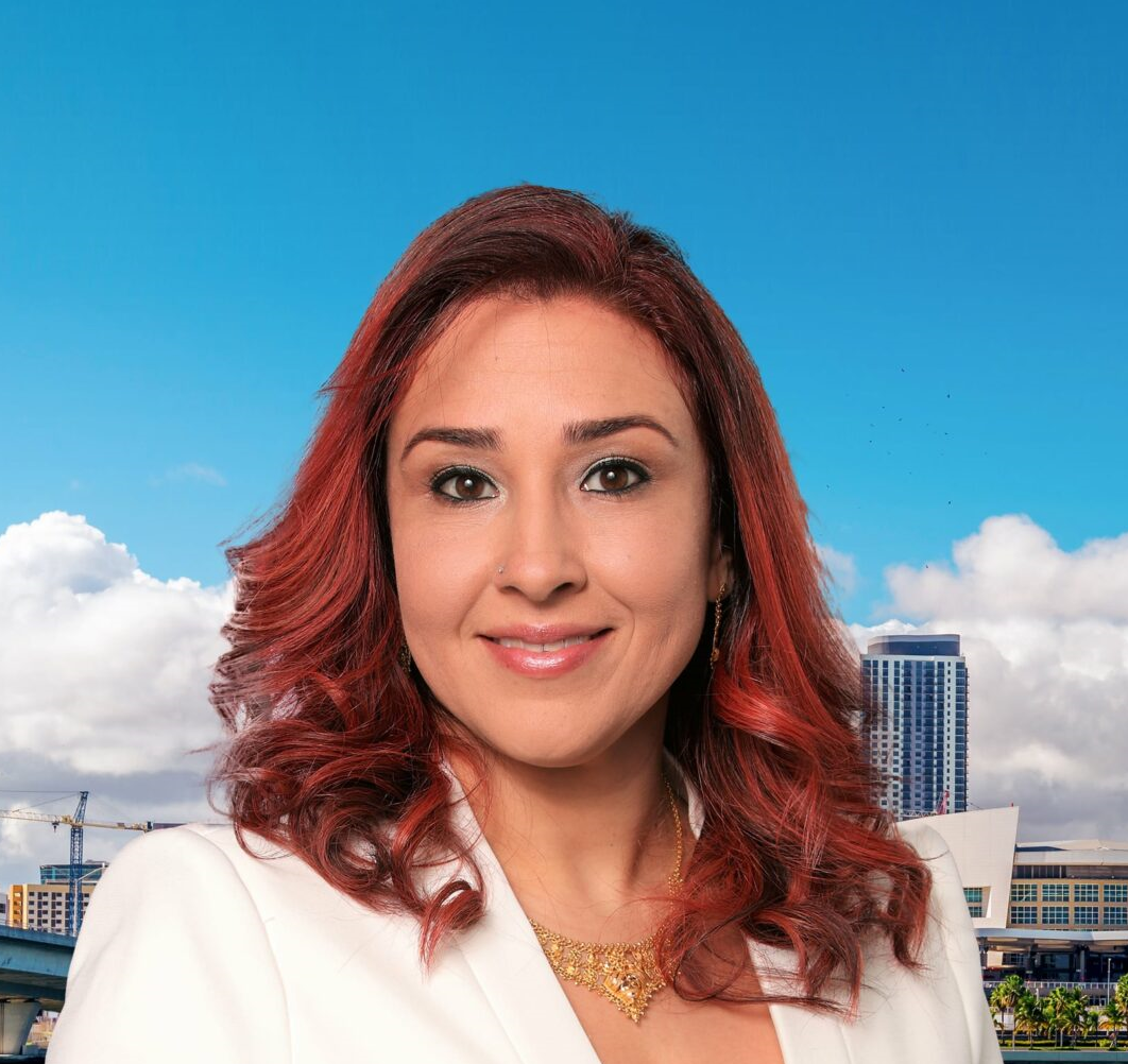 A woman with red hair is wearing a white jacket and a gold necklace.