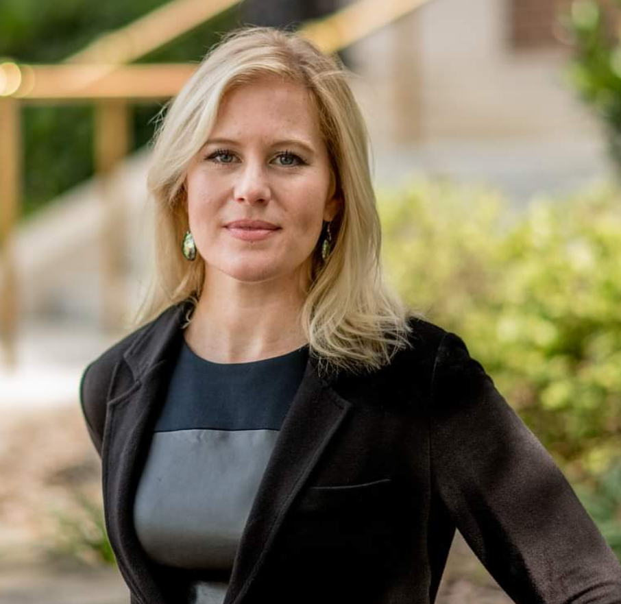 A woman wearing a black jacket and a black dress is posing for a picture.