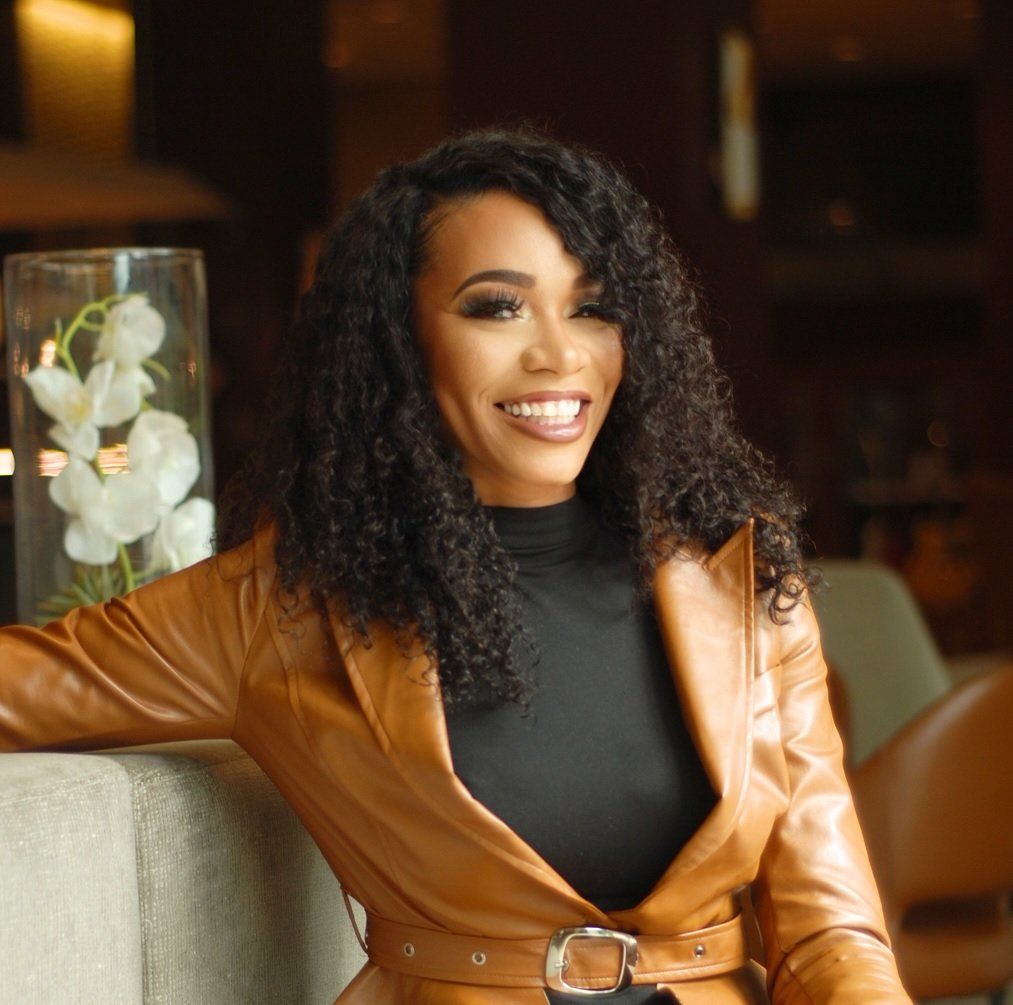 A woman in a brown leather jacket is smiling while leaning on a bar.