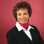A woman wearing a black suit and a pink scarf smiles for the camera
