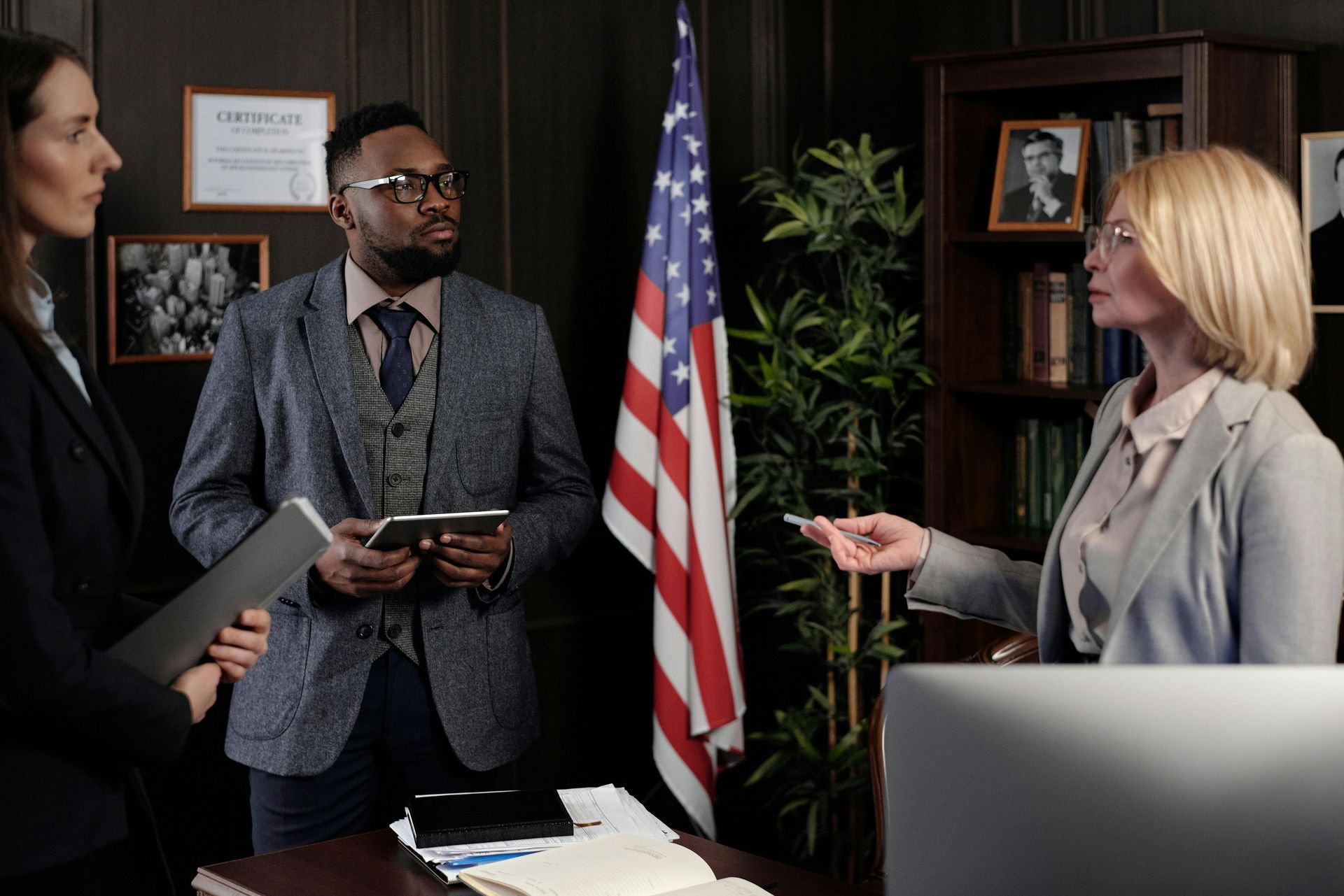 A group of people are standing in front of an american flag in an office.