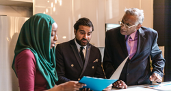 A group of people are sitting around a table looking at a clipboard.