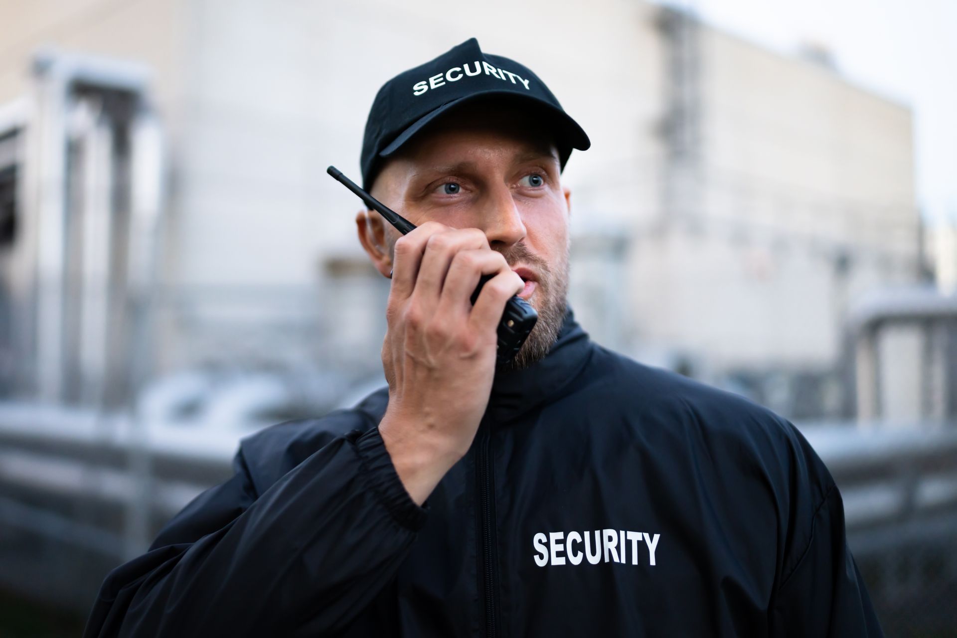 Security guard in uniform using a handheld radio in an urban setting.