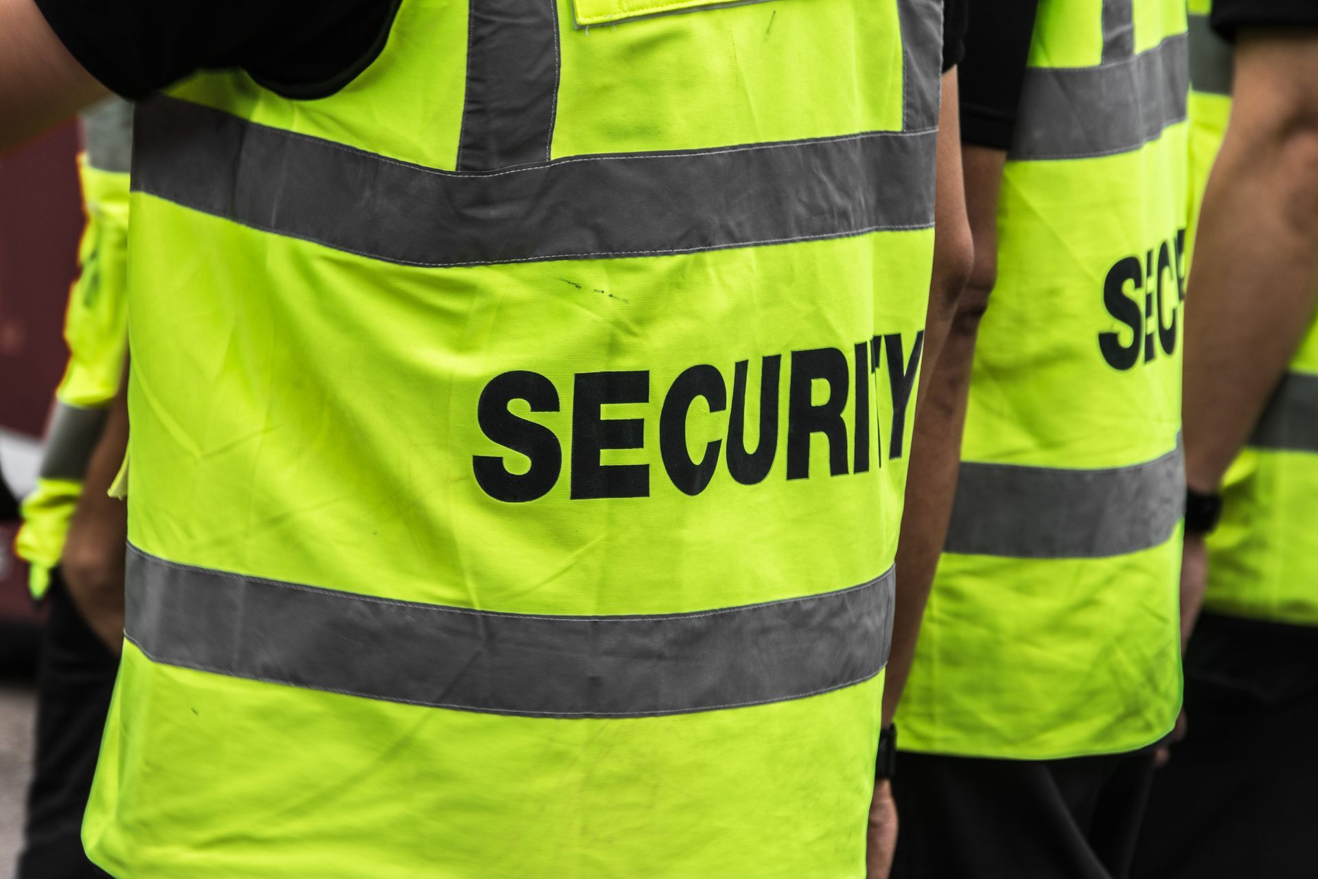 Security staff wearing high-visibility yellow vests with reflective stripes at public event outdoors.