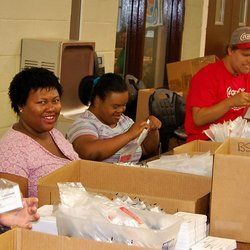 A group of people are sitting at a table packing boxes.