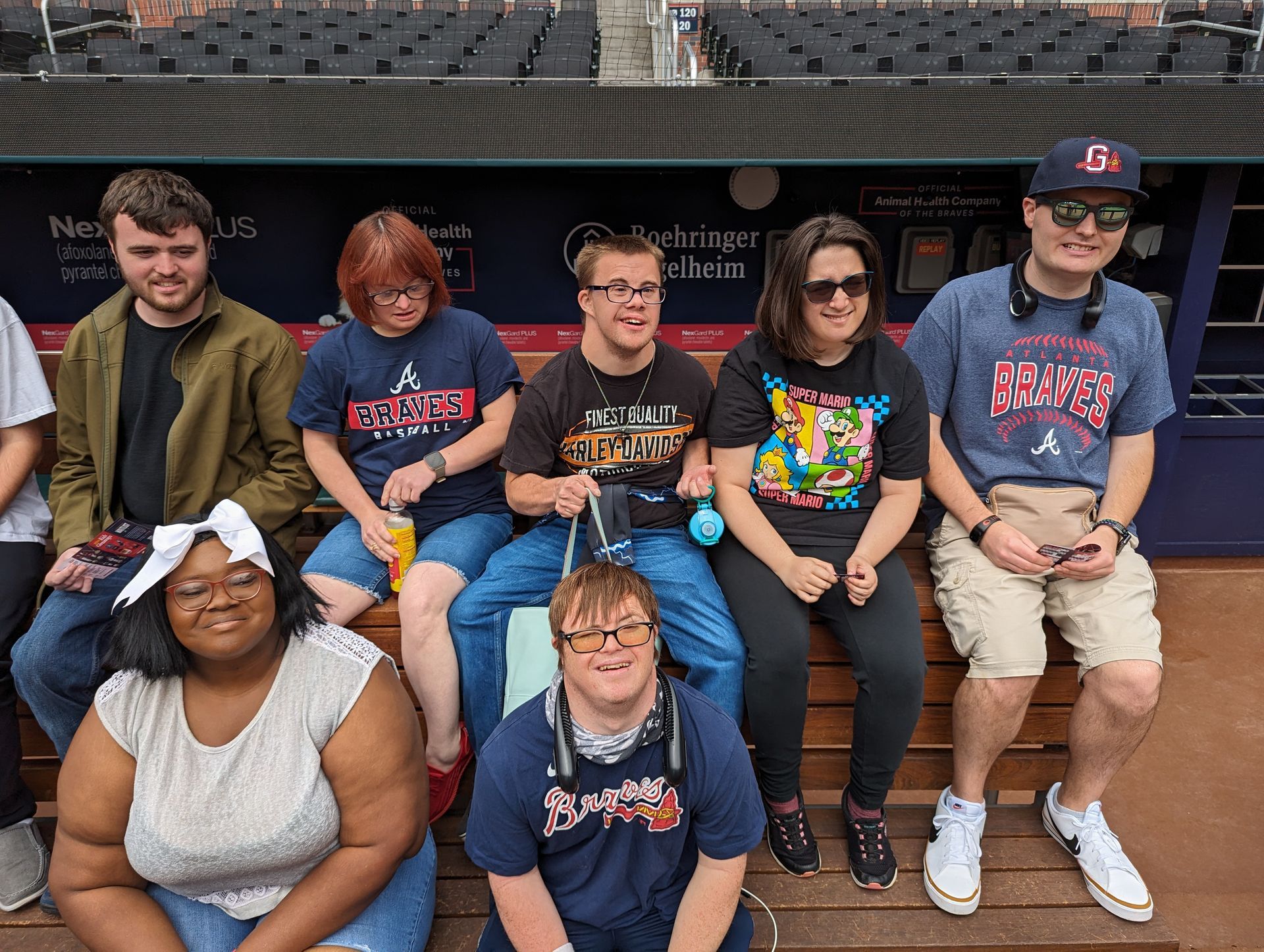 A group of people are sitting on a bench in front of a dugout.
