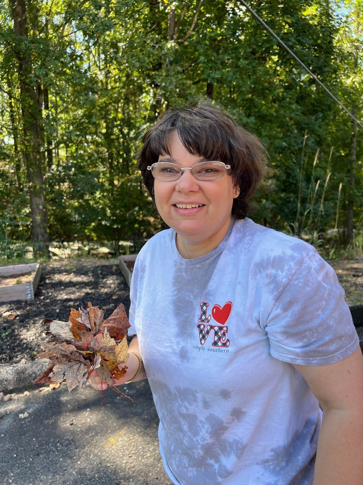A woman wearing glasses and a tie dye shirt is holding a bunch of leaves.