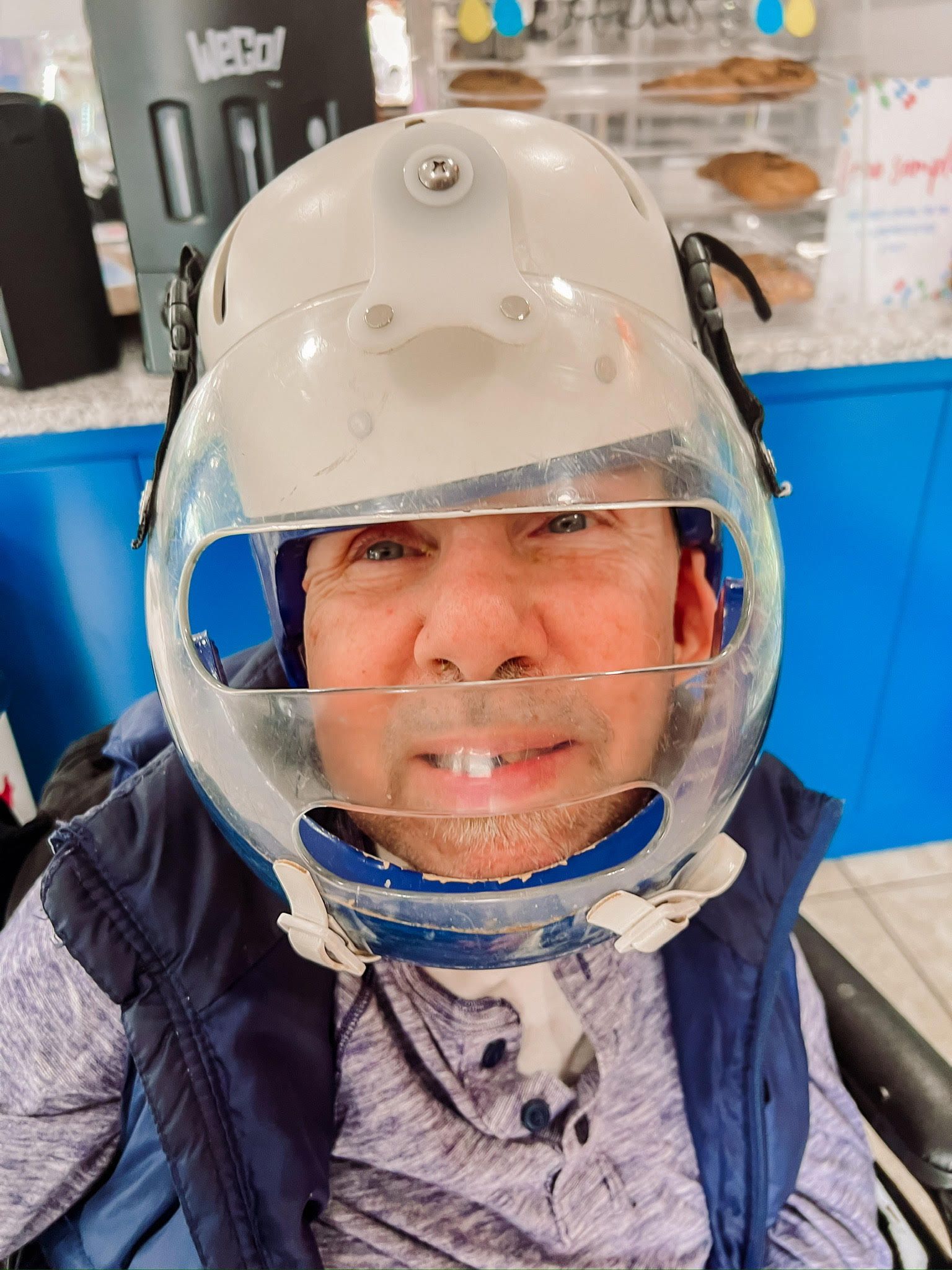 A man in a wheelchair is wearing a clear helmet on his head.