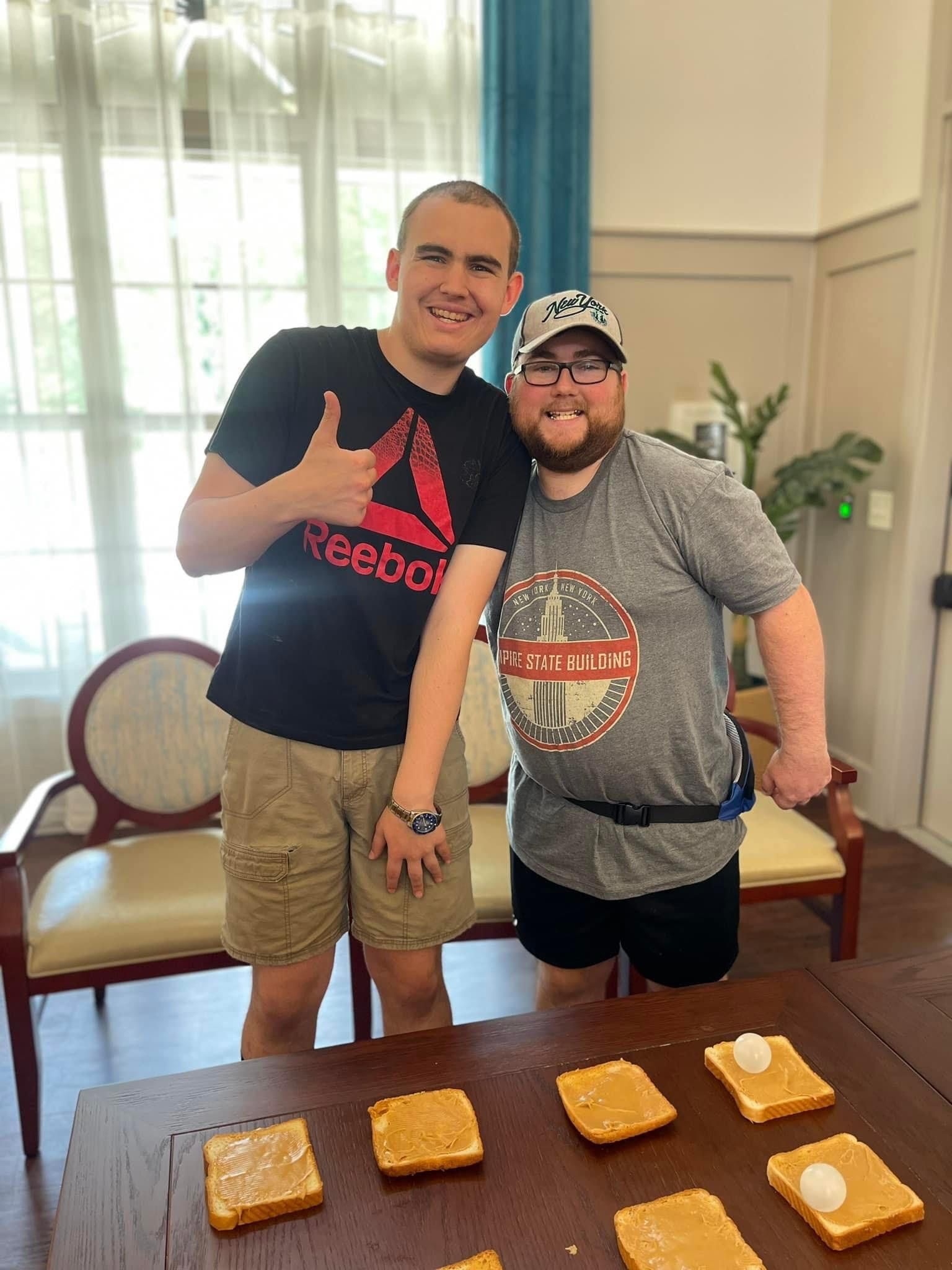 Two men are standing next to each other in front of a table with peanut butter sandwiches on it.
