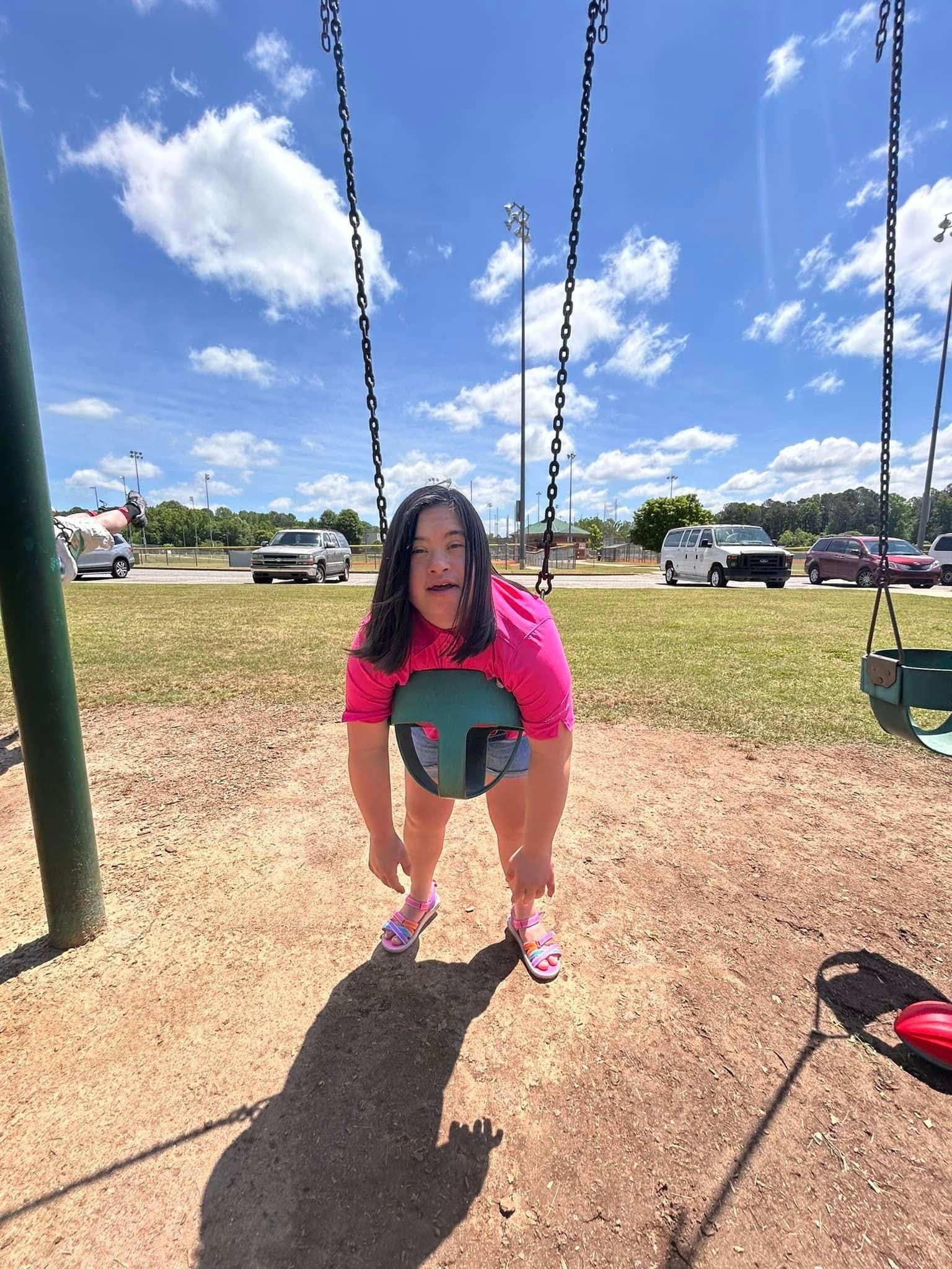 A little girl is sitting on a swing in a park.