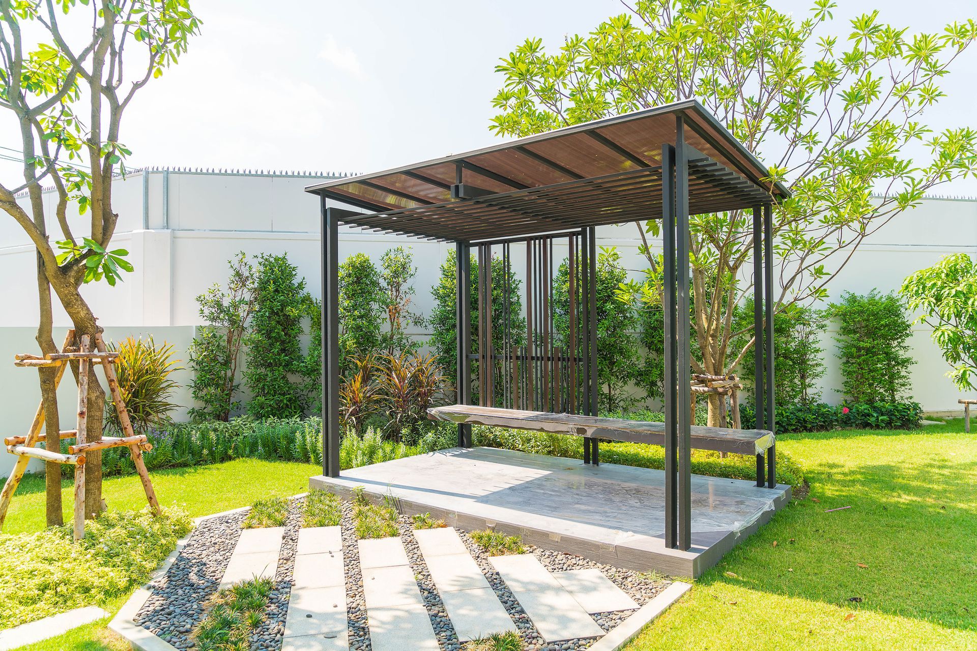 There is a pergola in the middle of the garden with a bench underneath it.