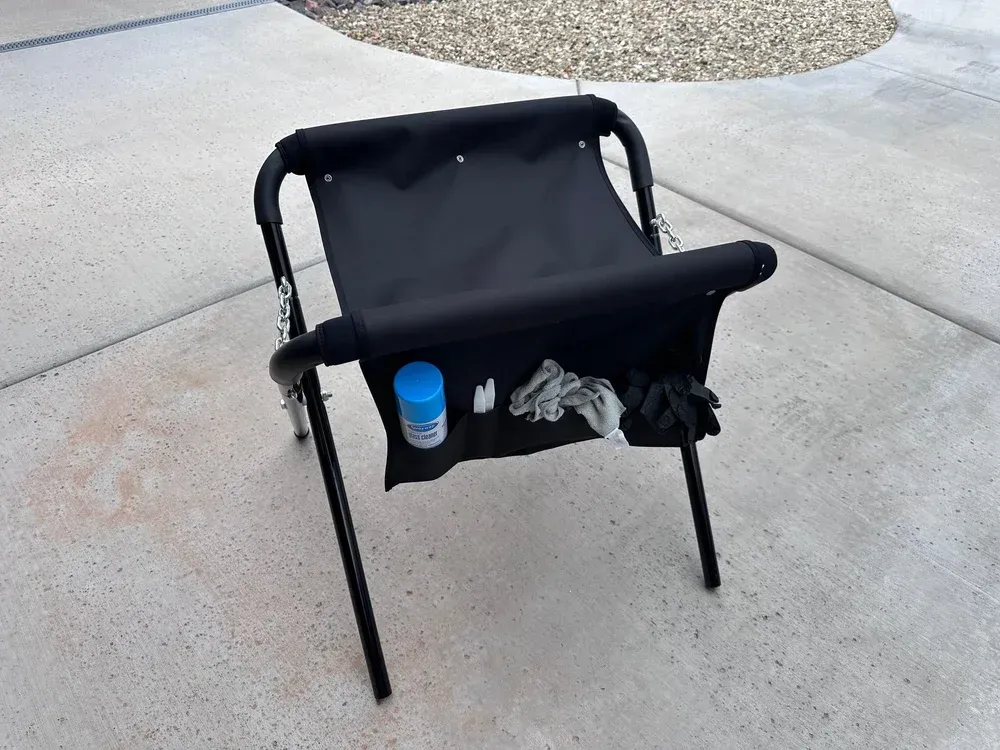 Black folding chair on a concrete driveway with a blue cup and gray gloves in the seat pocket.