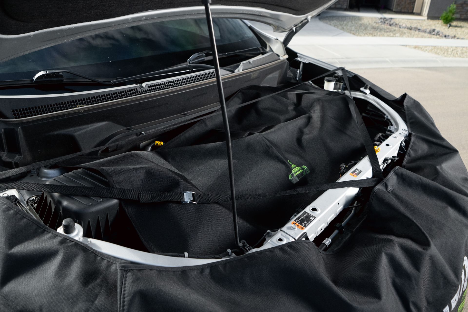 Black car with an open hood showing a custom Iron Hide hood cover