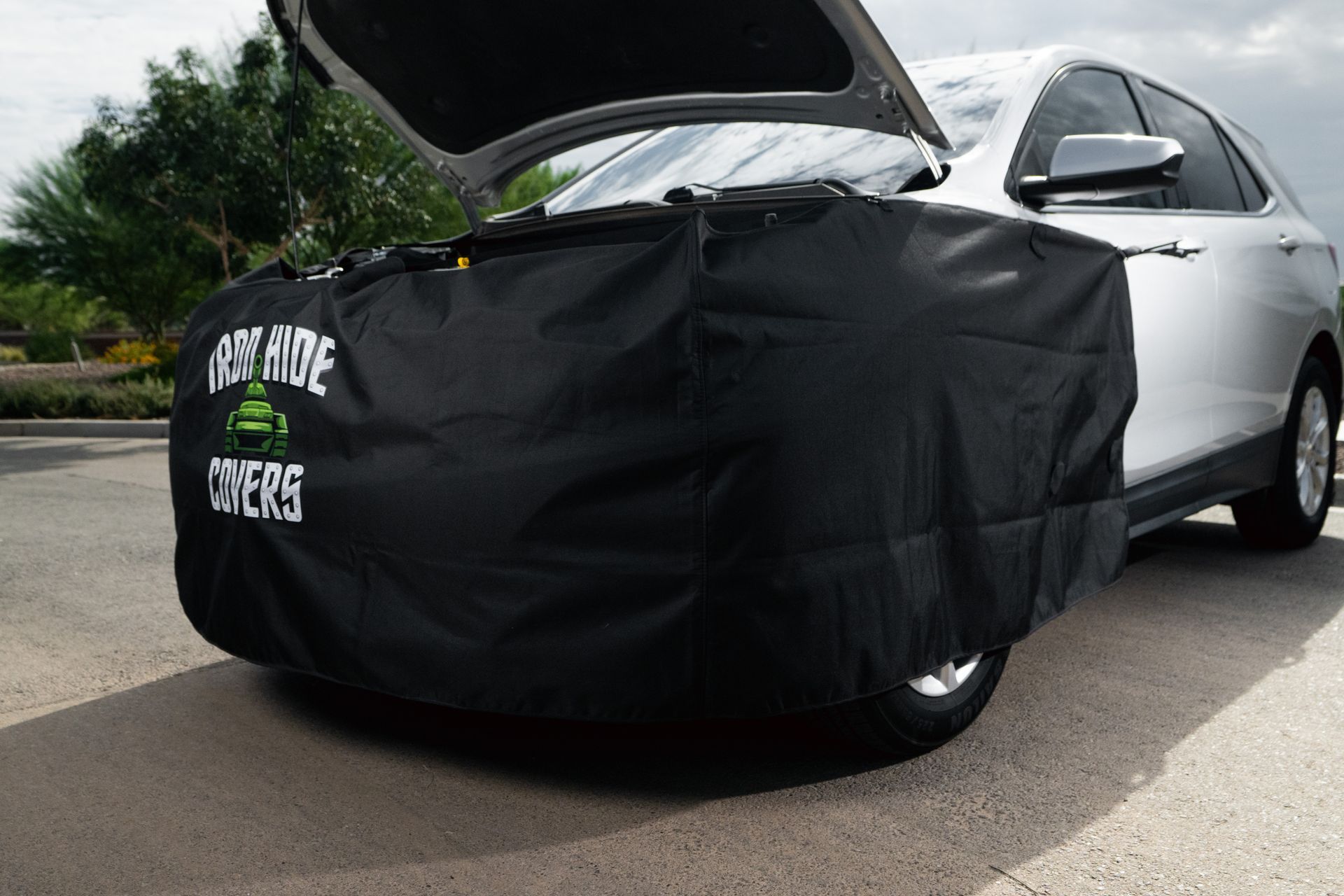 White car with hood and driver door open, front covered in black car cover on a suburban street.