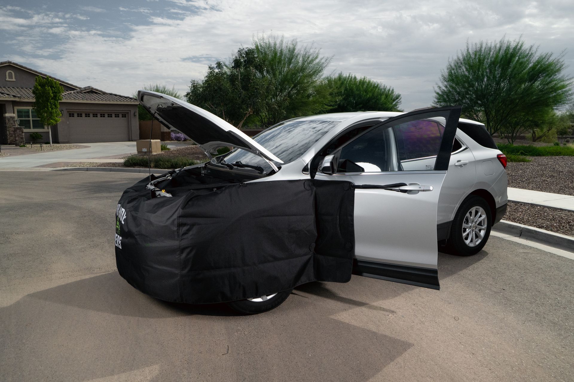 Car with front end covered in black Iron Hide cover, hood open and driver’s door open.