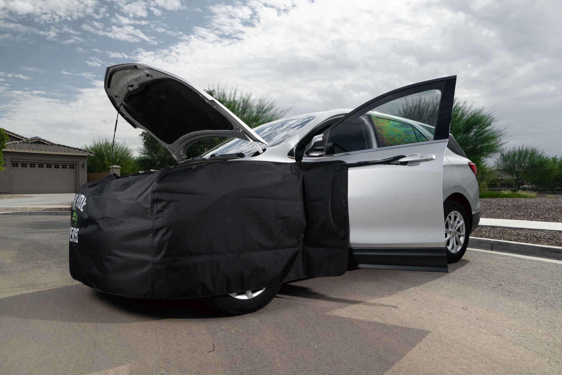 White car with hood and driver door open, front covered in black car cover on a suburban street.