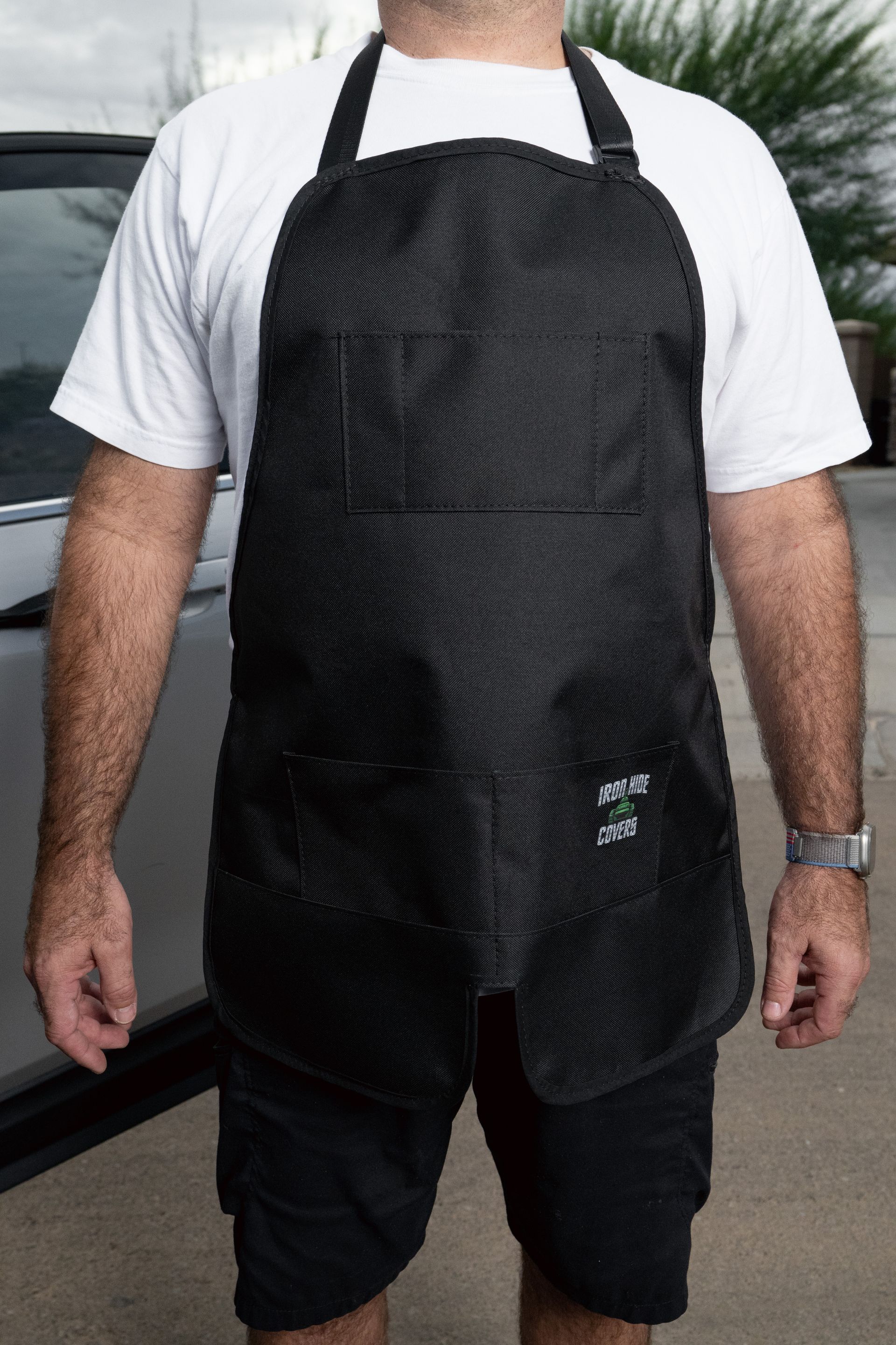 Person wearing a black apron over a white shirt and black shorts, standing outdoors.