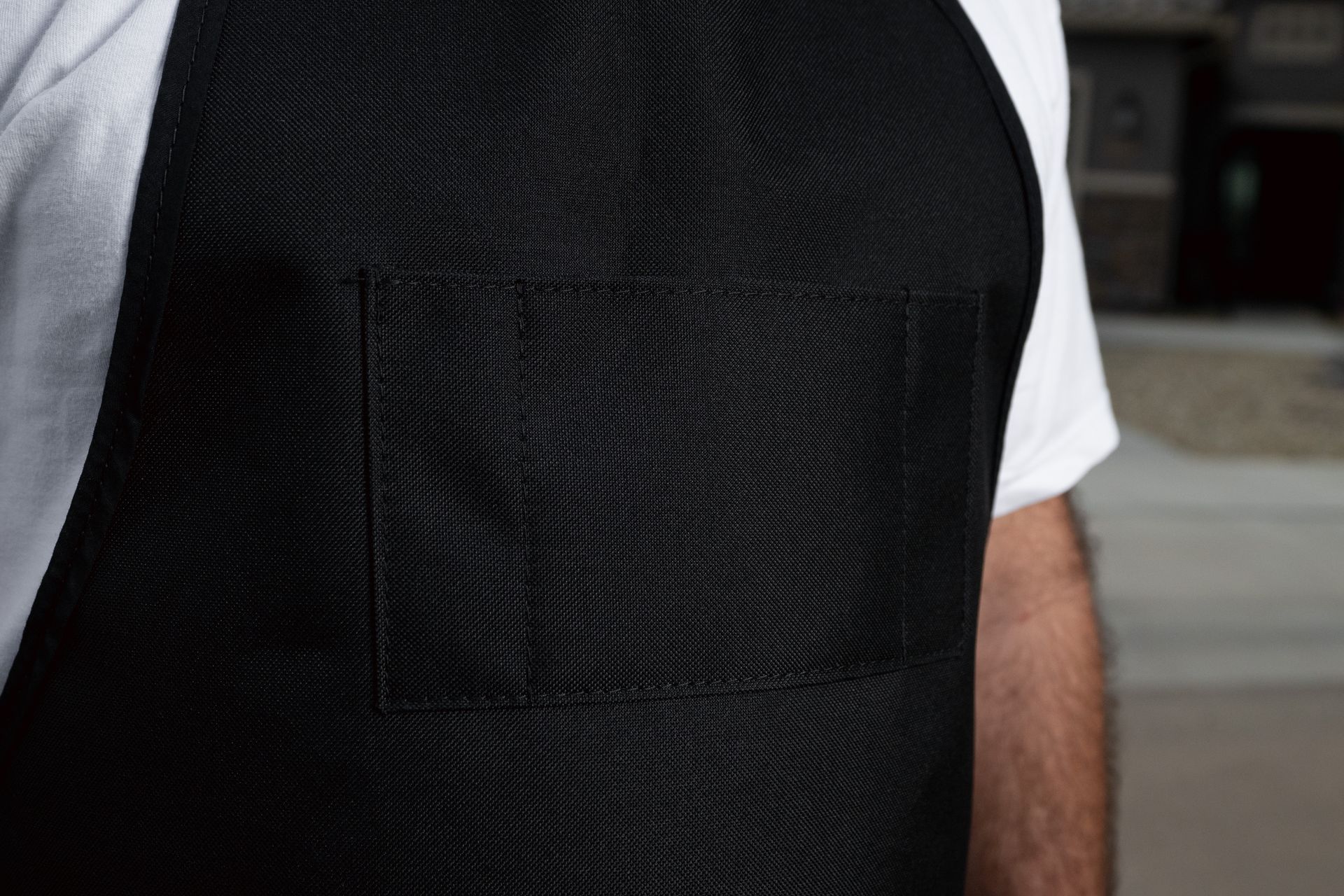 Person wearing a black apron over a white shirt and black shorts, standing outdoors.
