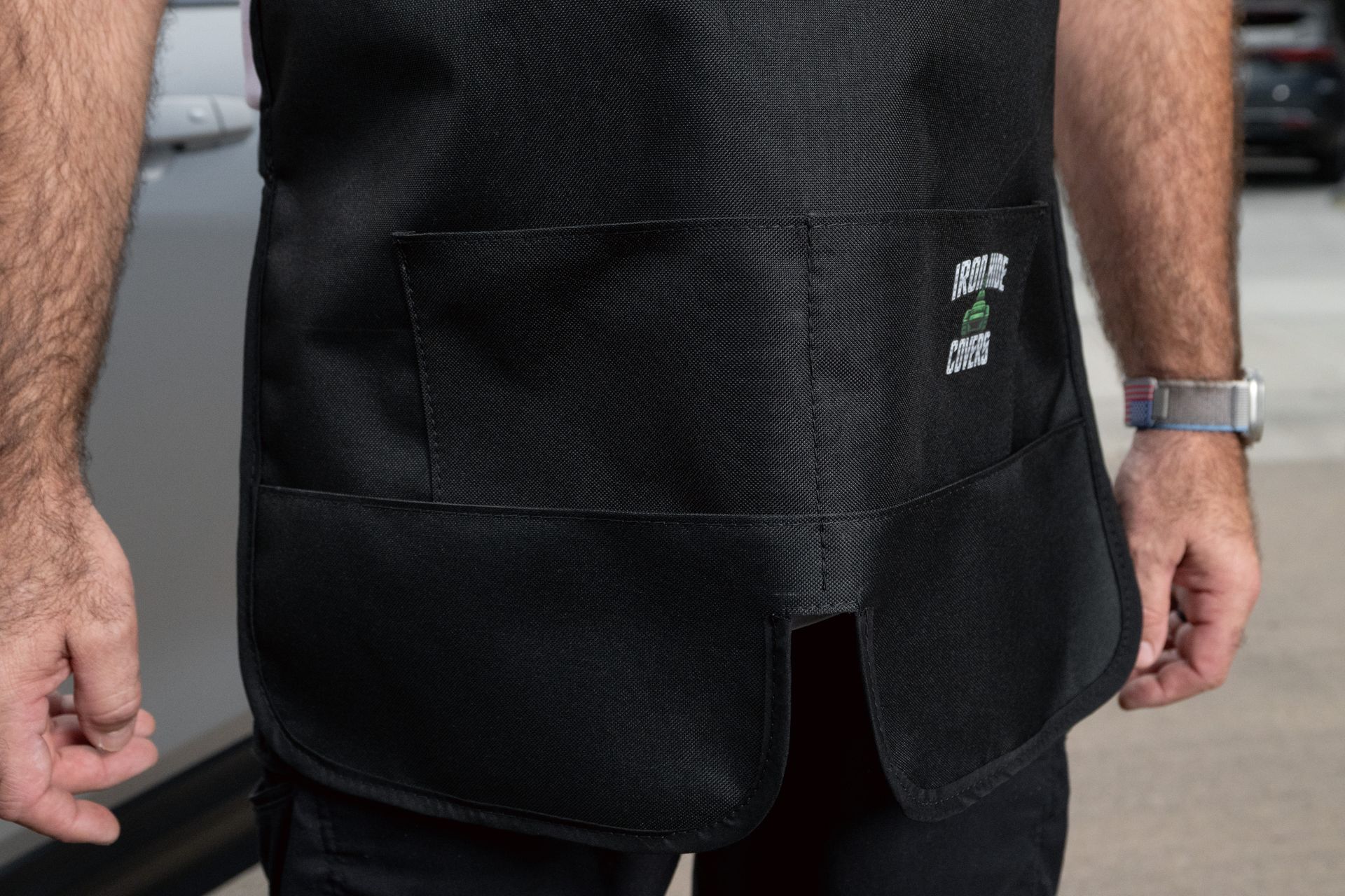 Person wearing a black apron over a white shirt and black shorts, standing outdoors.