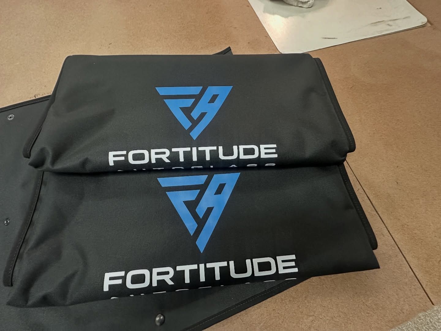 Two black Fortitude covers with blue logos and white text on a cardboard surface