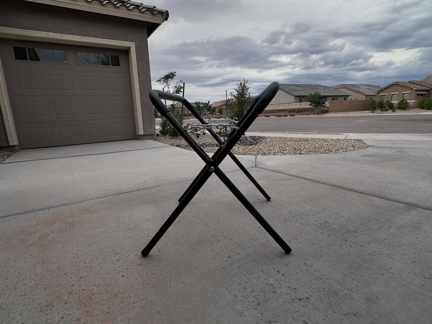 Black folding glass stand caddy on a suburban driveway, with a garage and houses in the background