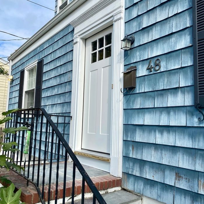 Blue shingled house with white door, black shutters, and black railing. House number is 48.