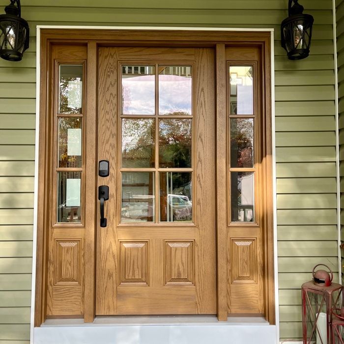 Wooden front door with glass panes and sidelights, flanked by black lanterns, on a green house.