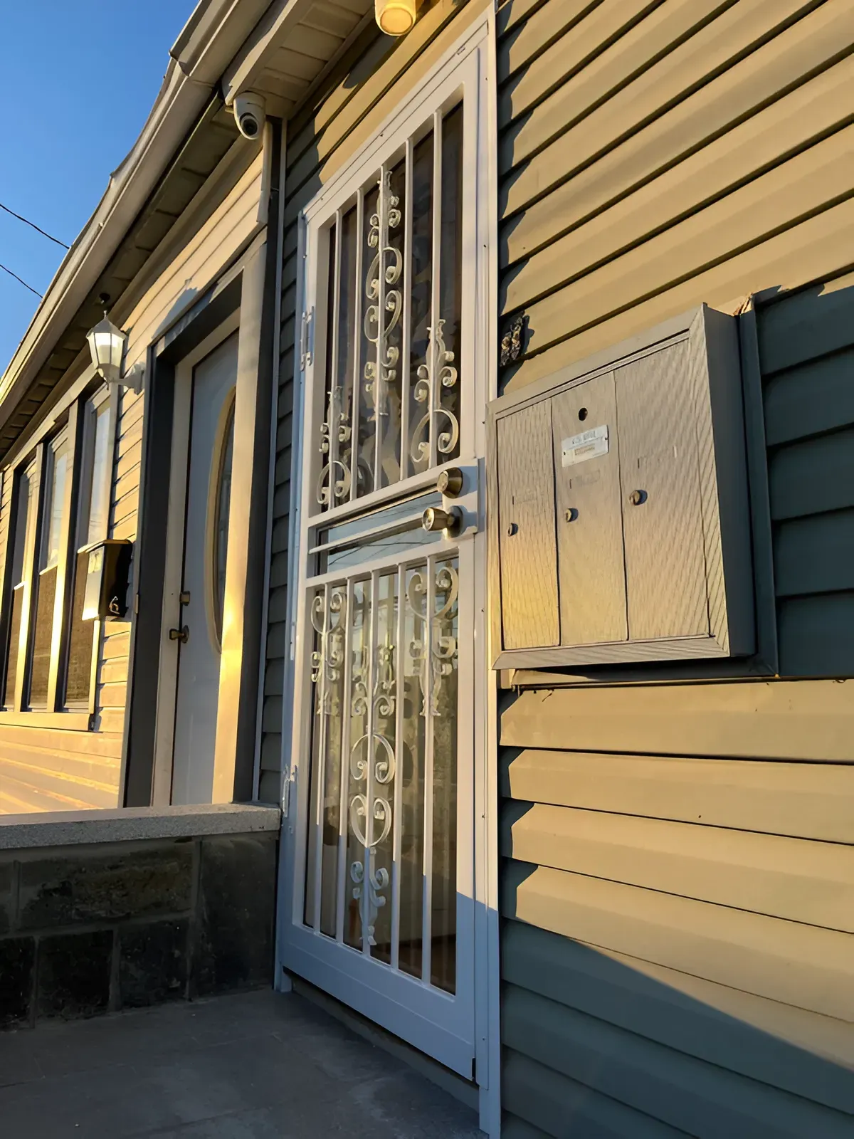 Exterior view of a house with a security door, mailbox, and green siding.